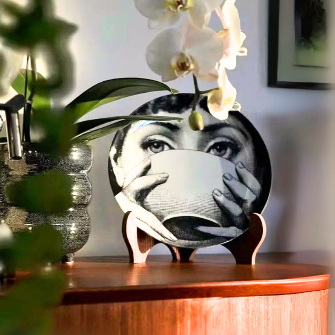 Decorative ceramic plate with a face design holding a cup on a wooden surface with plants.