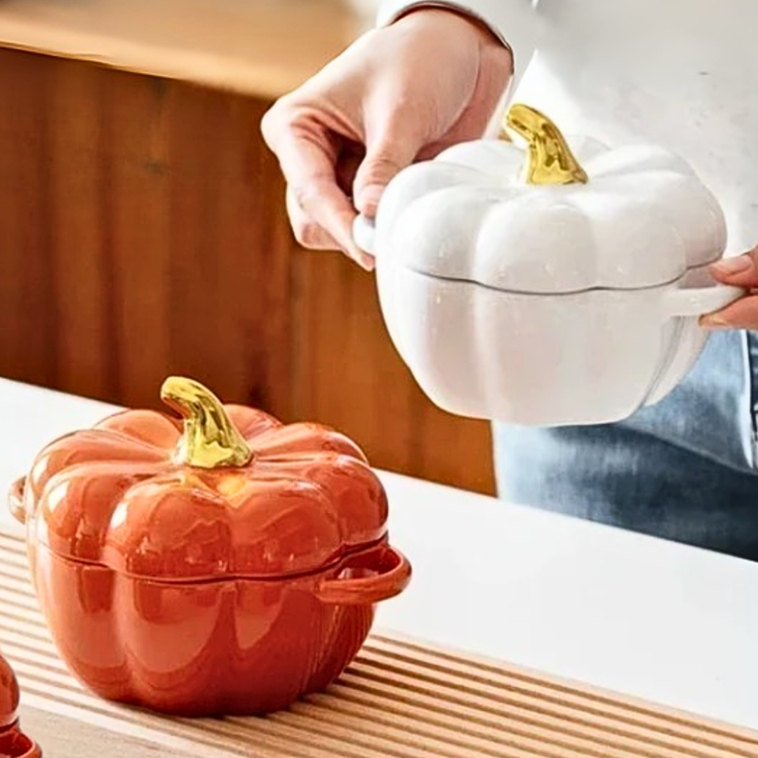 Two ceramic pumpkin-shaped soup bowls, one red and one white, on a wooden surface in a modern kitchen.
