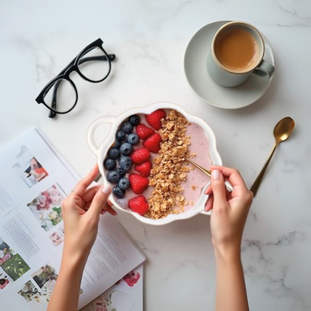 Person holding a bowl of cereal in a white pumpkin-shaped bowl with berries on a marble table with a cup of coffee and glasses.