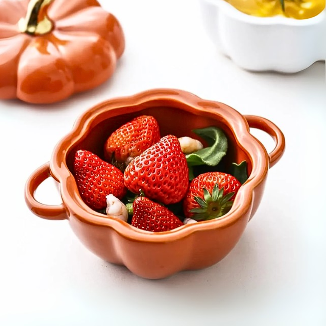 An orange pumpkin-shaped bowl with strawberries on a white kitchen countrer
