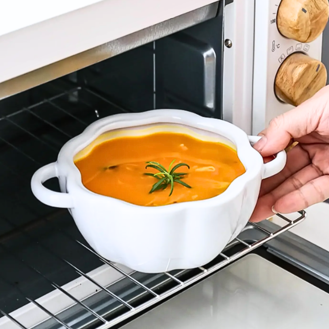 Person holding a bowl of soup with a white pumpkin-shaped ceramic bowl over an open microwave.