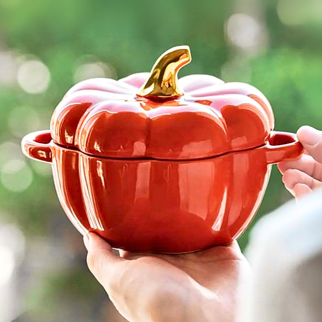 Orange ceramic bowl shaped like a pumpkin with a gold lid knob, held by a person against a blurred green backyard.
