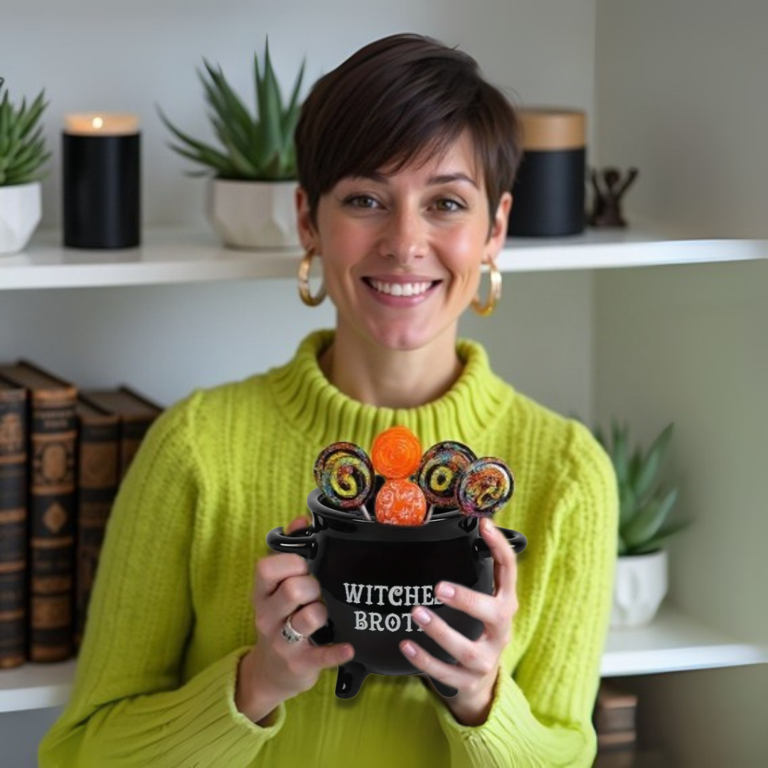 Woman holding a black cauldron-shaped container with Halloween candies, wearing a green sweater.