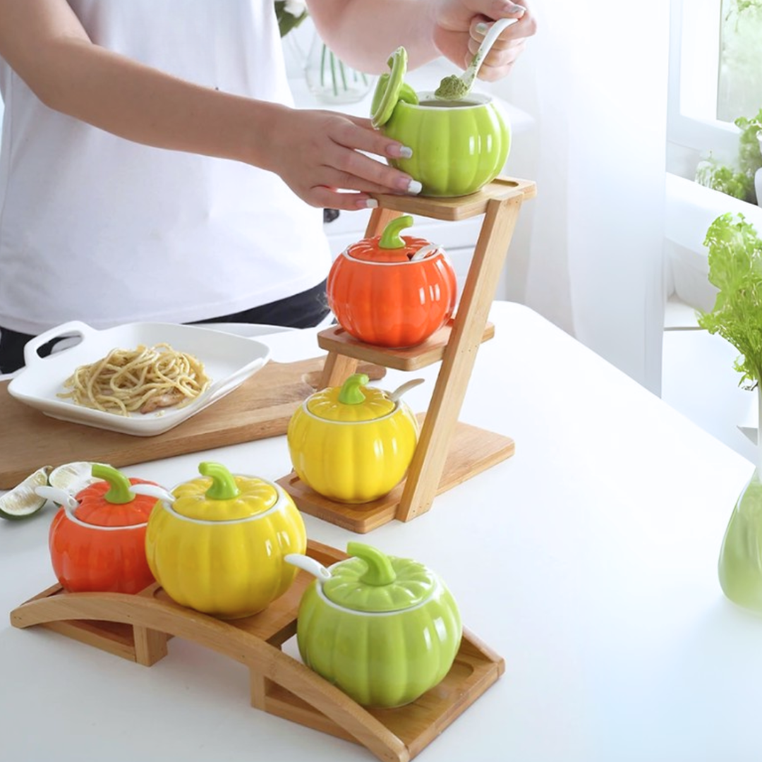 Colorful ceramic condiment containers shaped like pumpkins on a wooden stand.