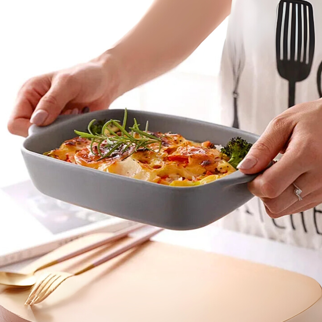 A person holding a gray ceramic dish with pasta and greens in a modern kitchen