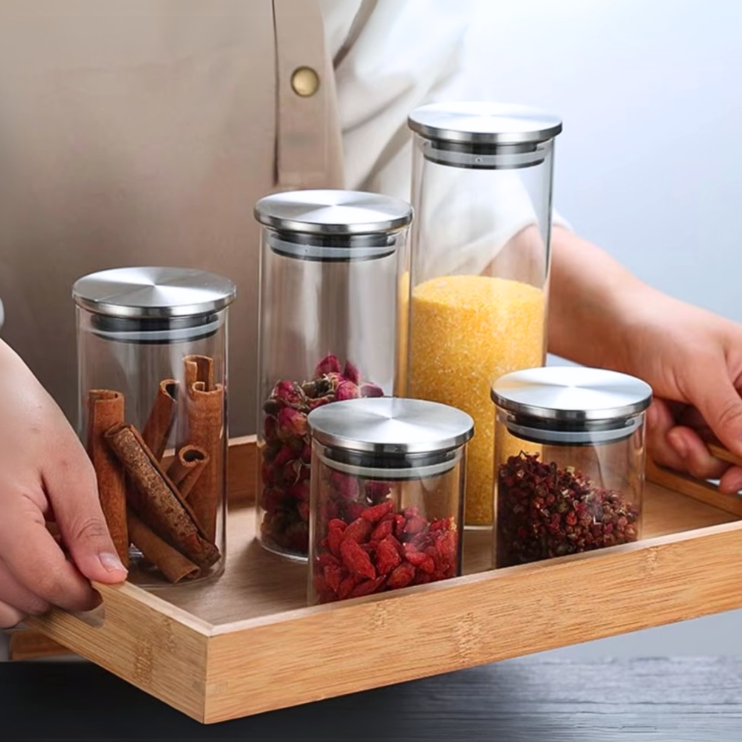 Glass jars with stainless steel lids on a wooden tray, containing spices.