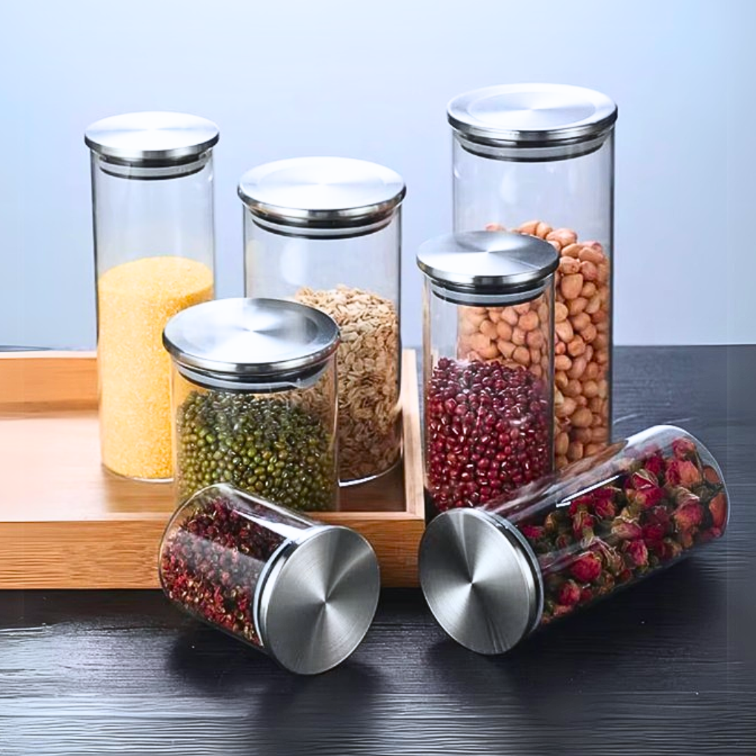 Set of glass jars with airtight stainless steel lids containing various dry foods on a wooden tray.