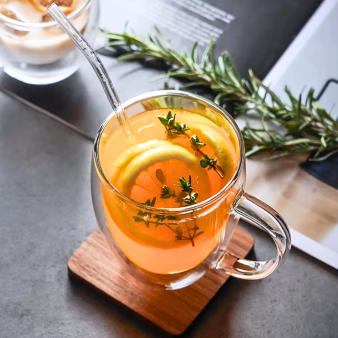 Clear mug with hot beverage, lemon slice, and herbs on a wooden coaster.