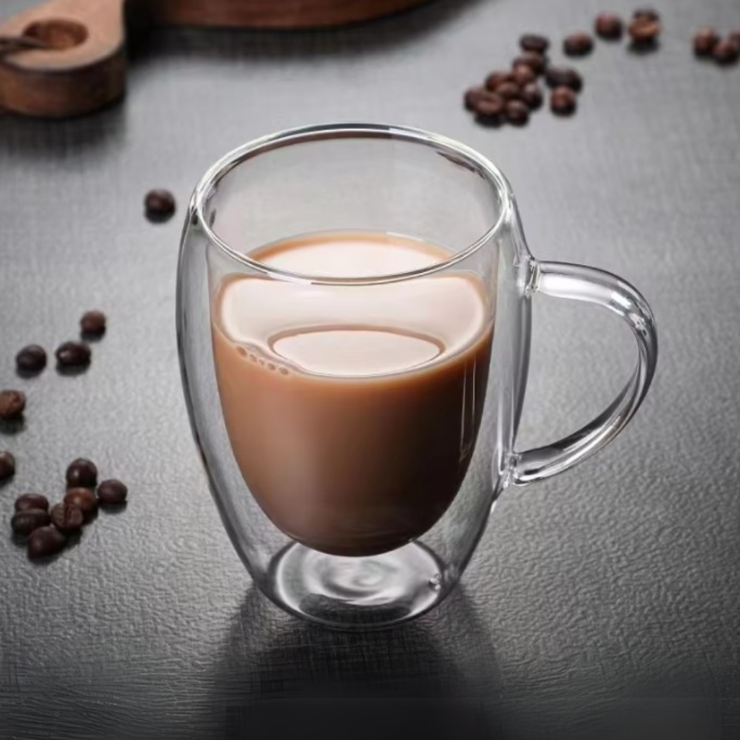 Clear glass mug with layered coffee and milk on a dark surface with scattered coffee beans.
