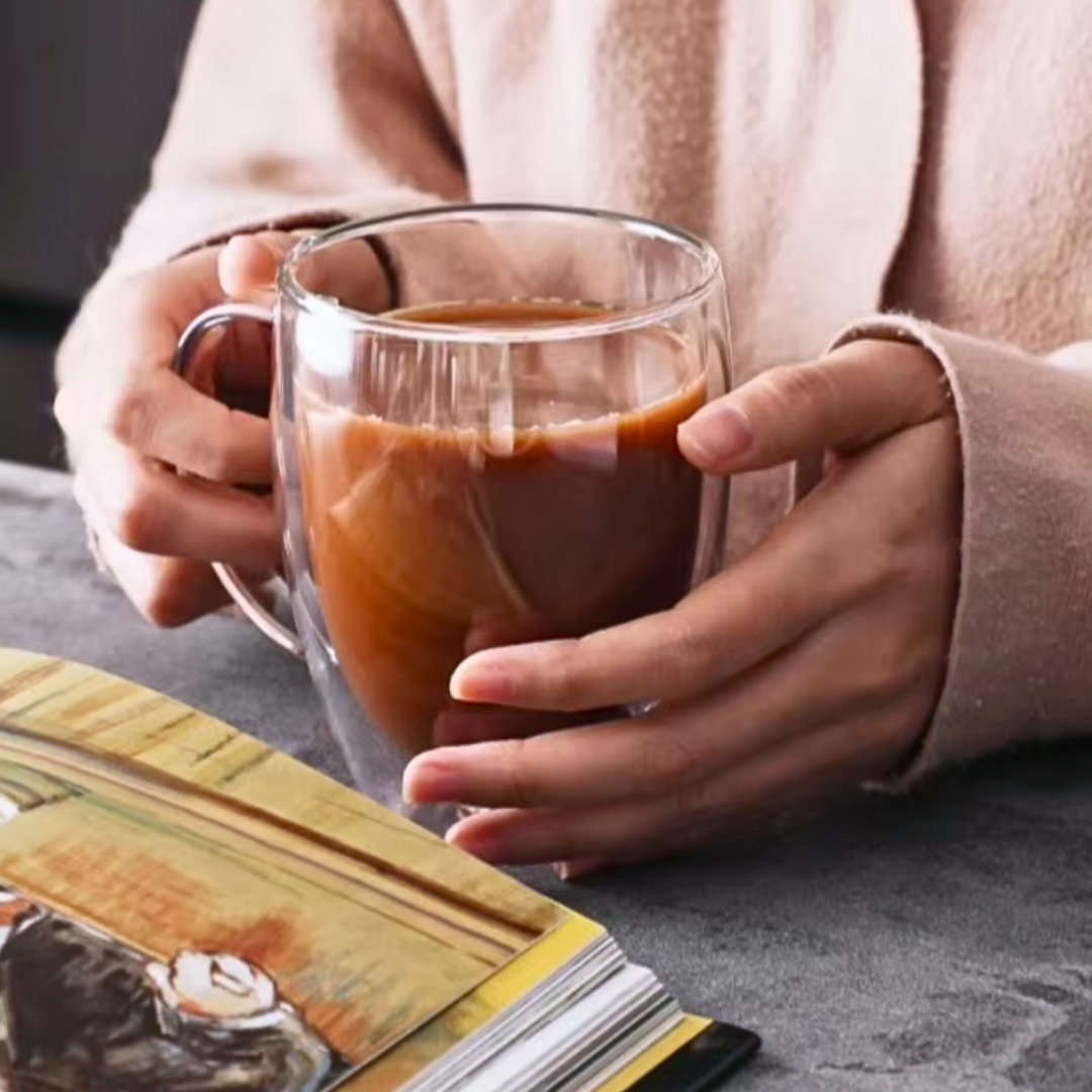 Person holding a glass mug of coffee with a book on a table