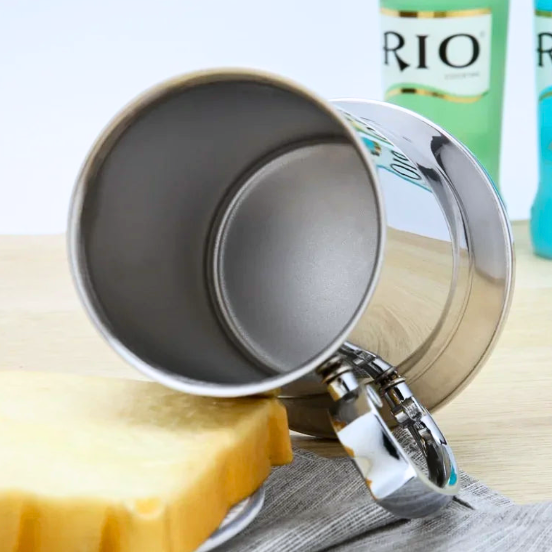 A stainless steel cup on a wooden table with bottles in the background