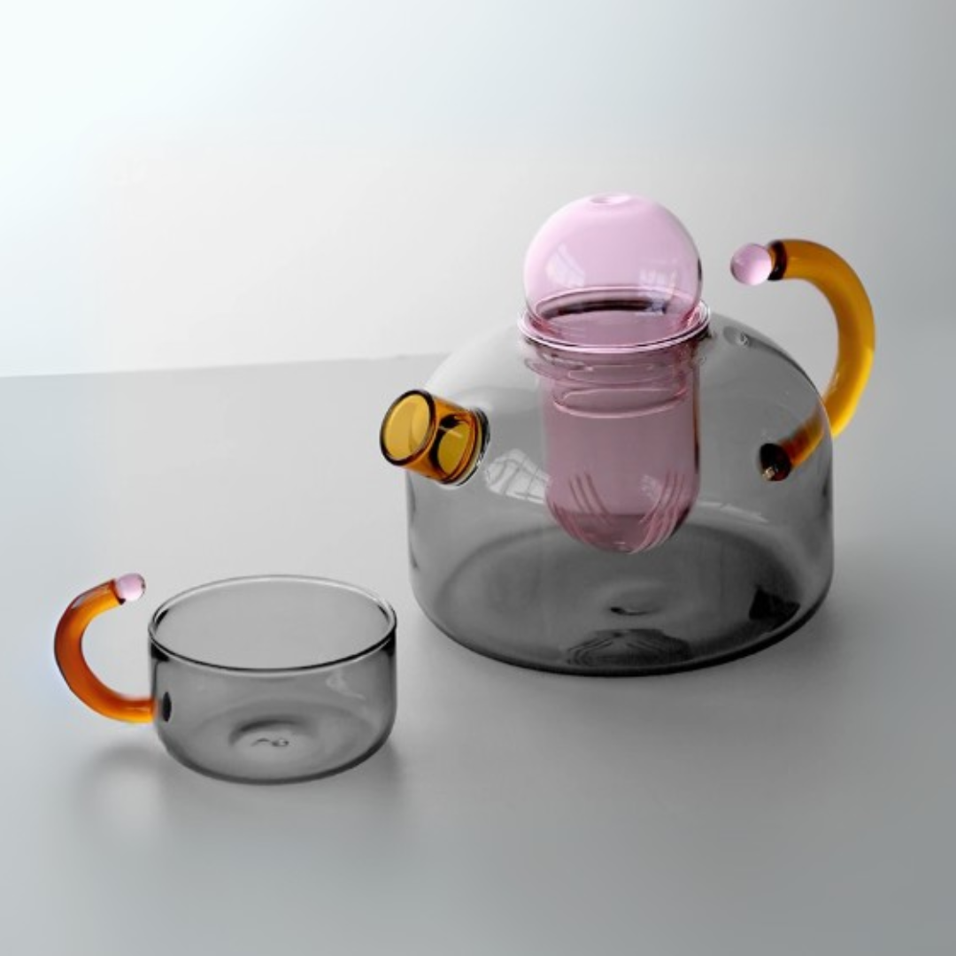 Clear glass teapot with pink interior and orange handles and a matching cup