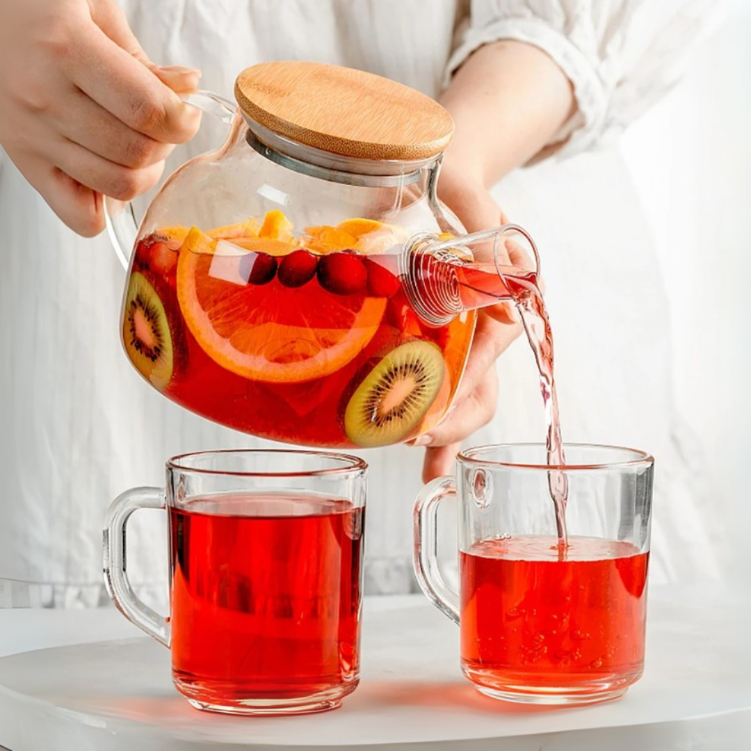 Person pouring fruit-infused water from a glass pitcher into two clear mugs