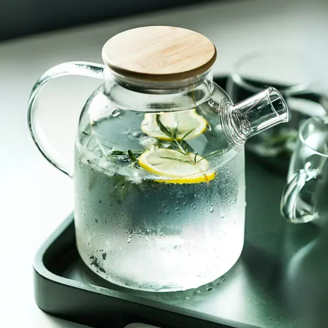 Clear glass kettle with wooden lid on a dark tray