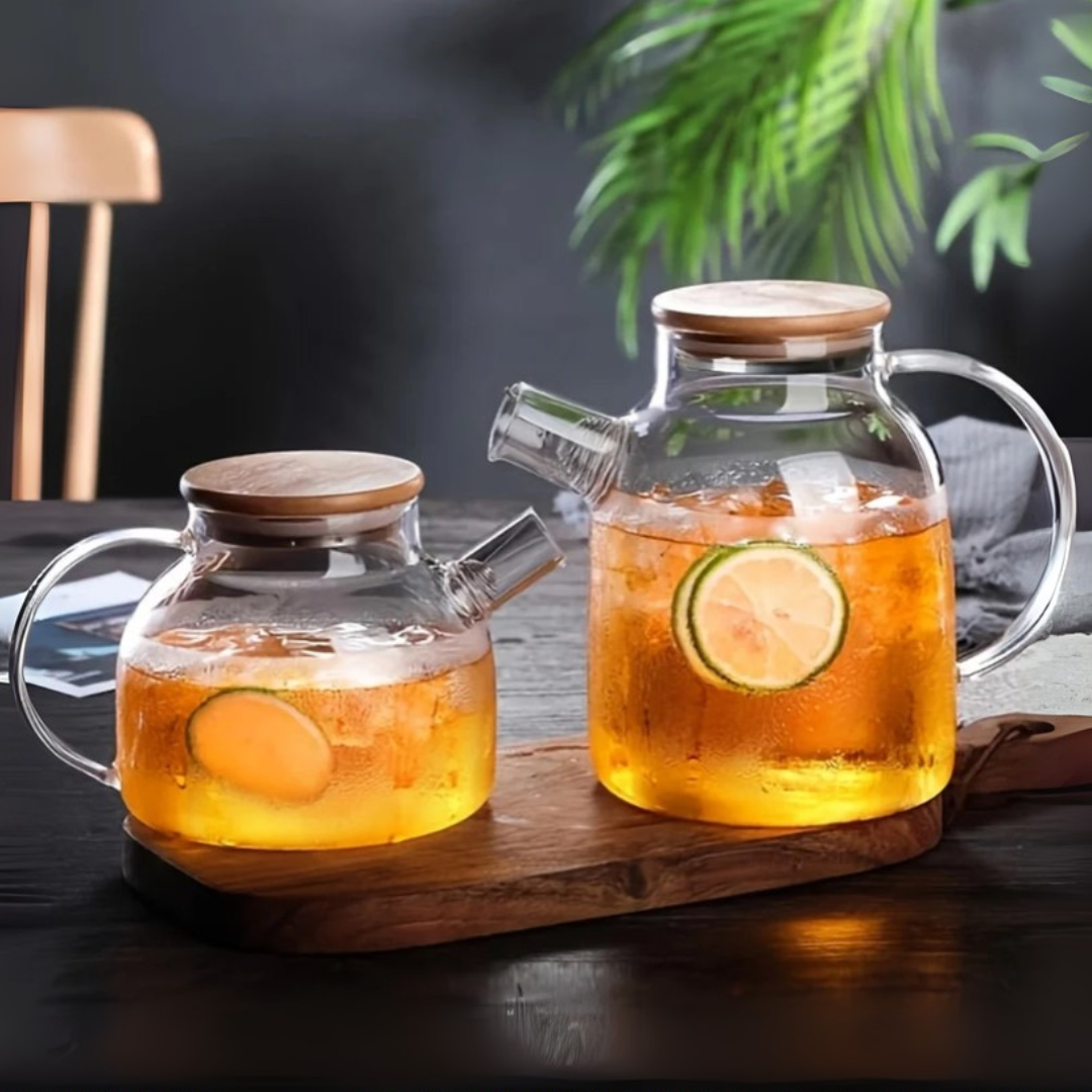 Two glass kettles with a wooden lid on a wooden tray, containing ice tea with slices of fruit.