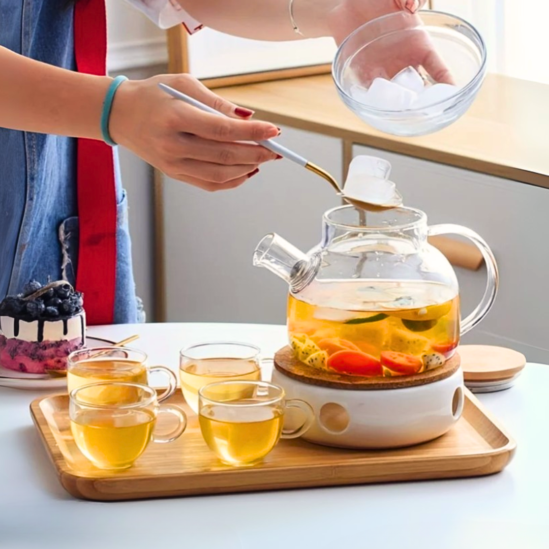 Person preparing a glass kettle with ice, fruit and cups on a wooden tray.