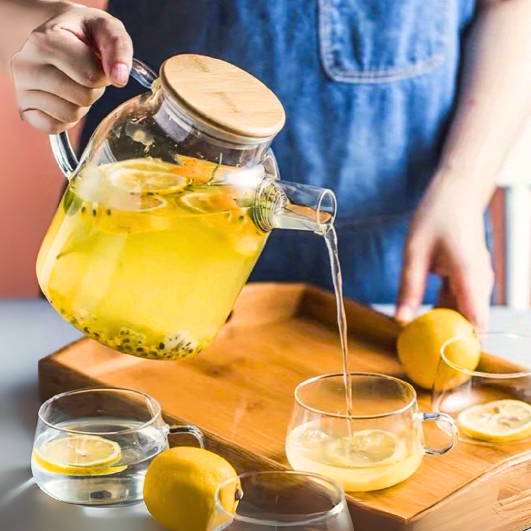 Person pouring lemon tea from a glass kettle into a cup on a wooden tray.