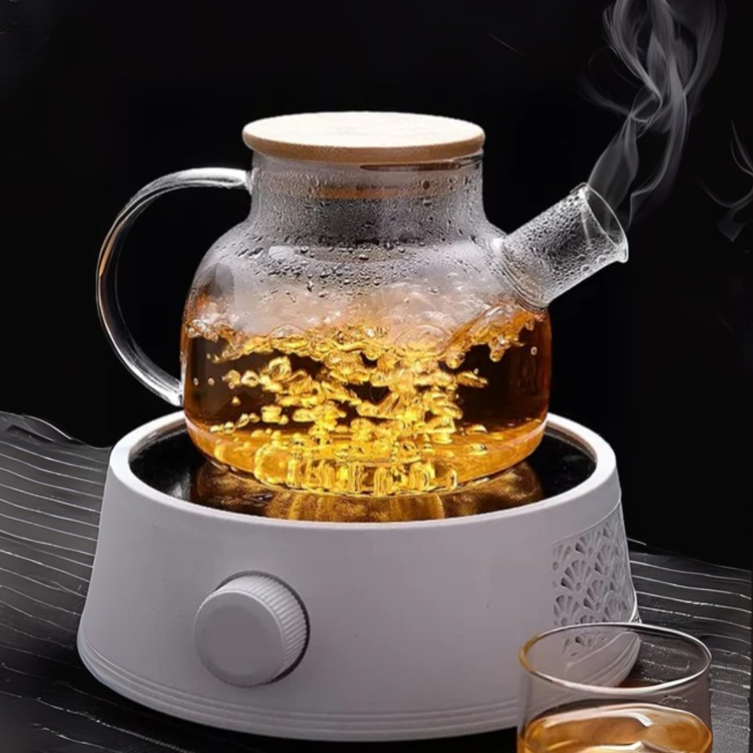 Glass kettle with wooden lid on an electric stove, filled with steaming tea.
