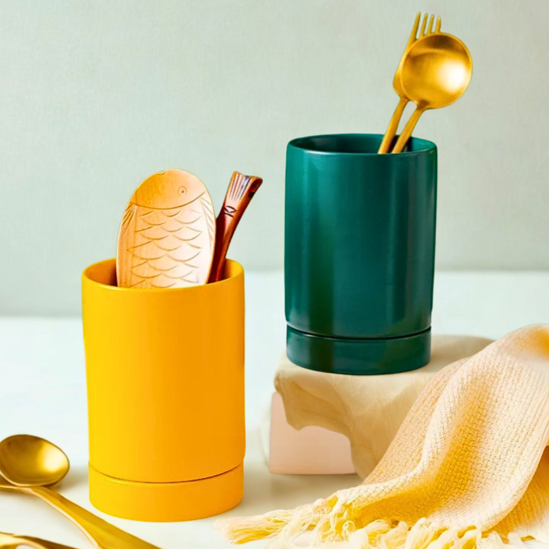 Two colorful ceramic utensil crocks with gold utensils on a bright table.
