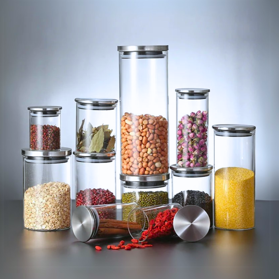 Set of glass storage jars with airtight stainless steel lids containing various dry goods on a gray table.